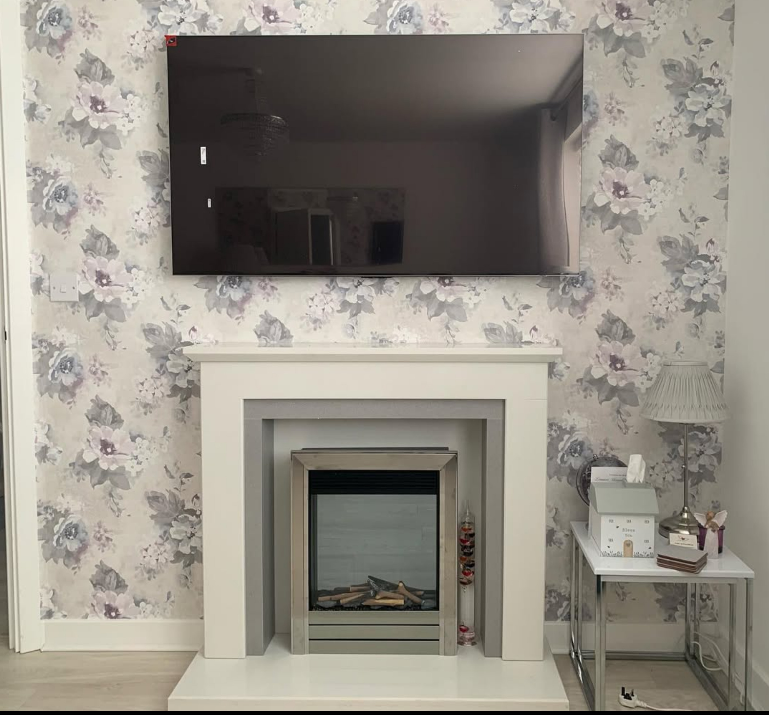 TV wall mounted above modern fireplace with floral wallpaper